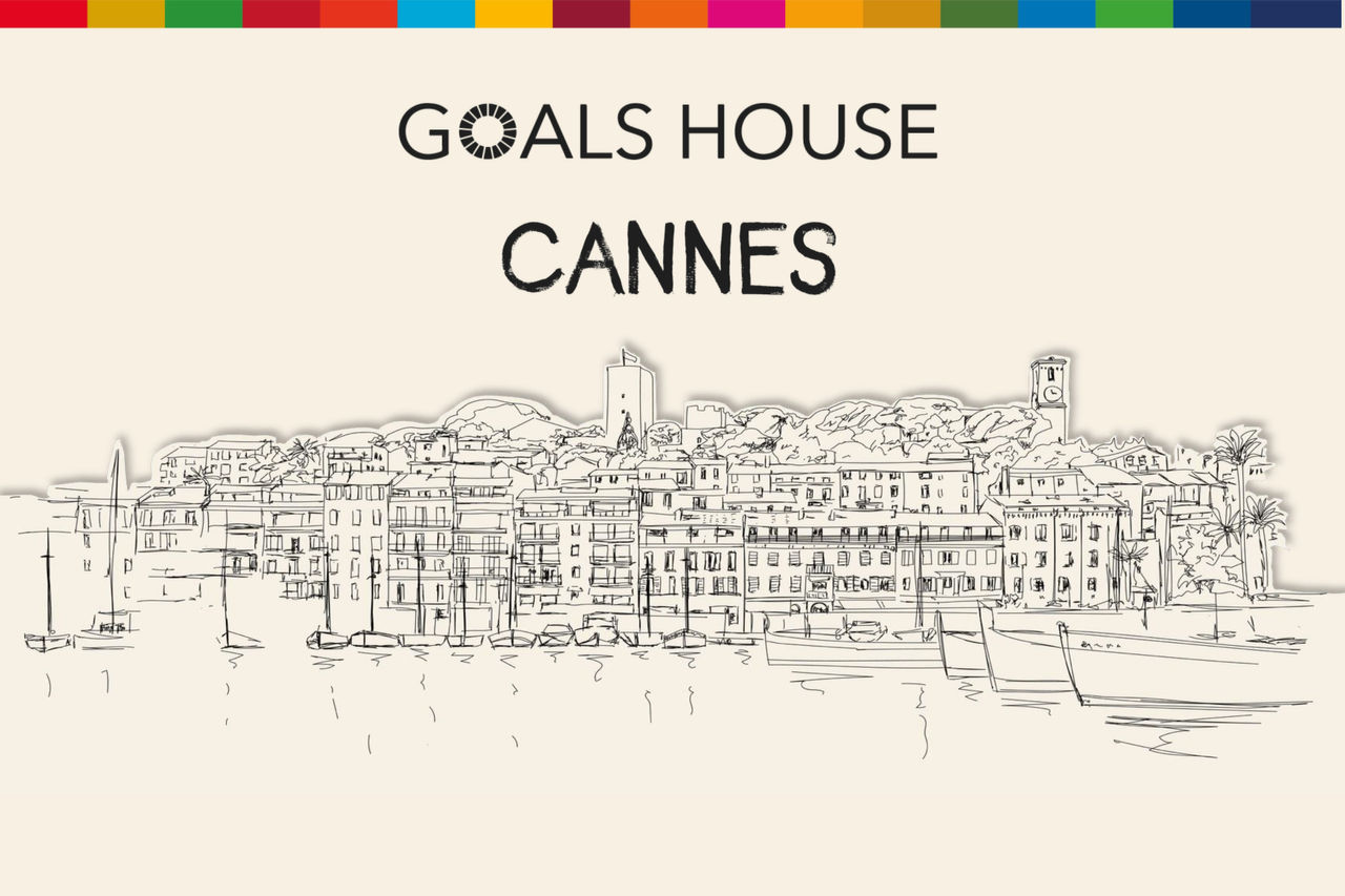 An illustration on a warm off-white background drawn in pencil of the Cannes, France cityscape, as seen from the water. A heading sits above the drawing that says "Goals House" on the first line and "Cannes" on the second line. A striped band of various colors runs along the top of the image.